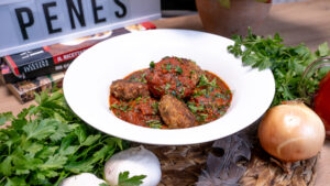 Chifteluțe din carne de curcan, acoperite cu sos de roșii aromat și decorate cu pătrunjel proaspăt, servite într-un bol alb, alături de usturoi și pătrunjel.
