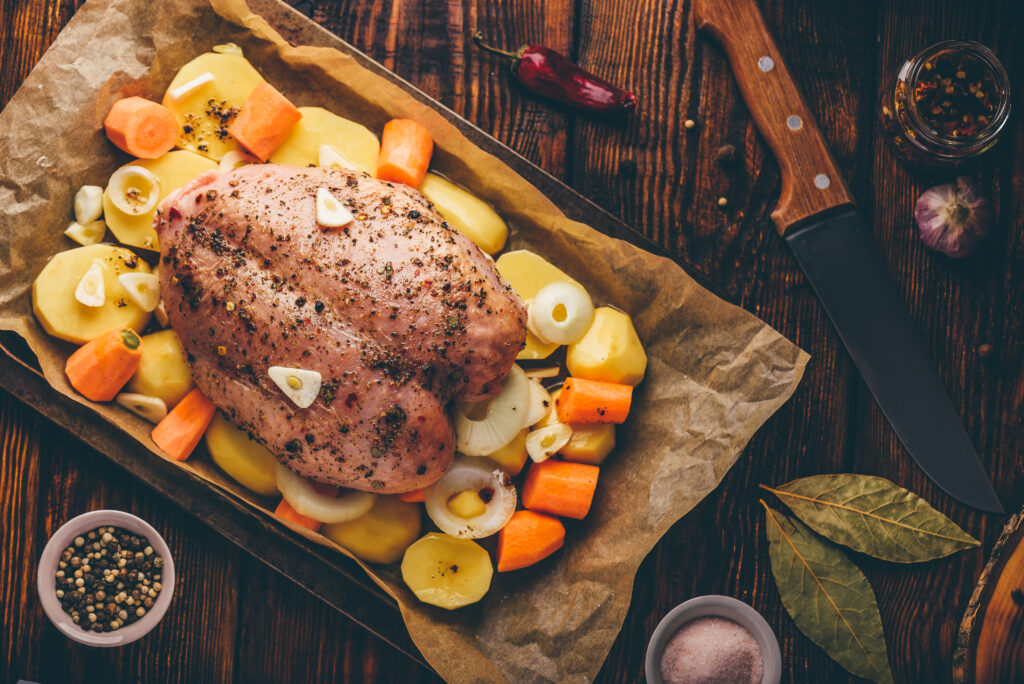 Piept de curcan rumenit la cuptor, așezat peste un pat de legume proaspete, incluzând morcovi și cartofi, pregătit pentru o masă sănătoasă și delicioasă