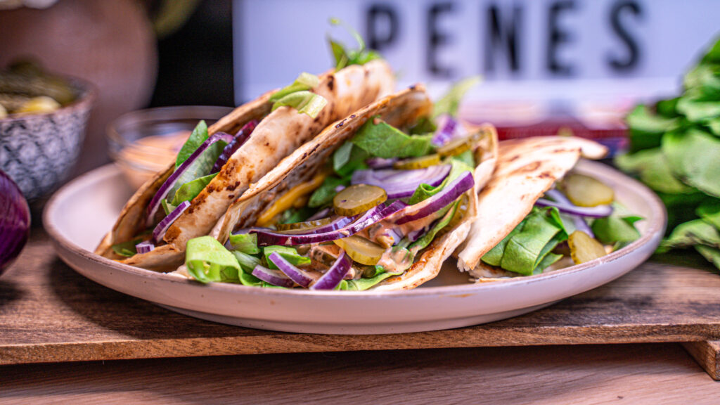 Cheeseburger Taco de Curcan cu salată verde, ceapă roșie și castraveți murați, servit pe o farfurie.
