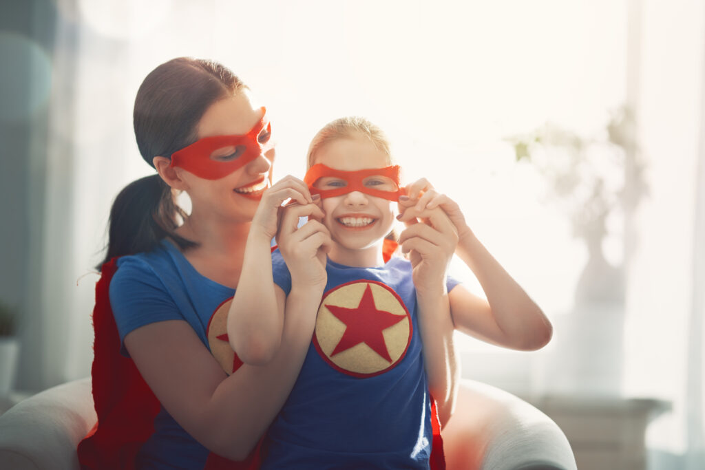 Mamă și fiică zâmbitoare în costume de supereroi, simbolizând părinții care cresc copii sănătoși cu ajutorul produselor Peneș Curcanul.