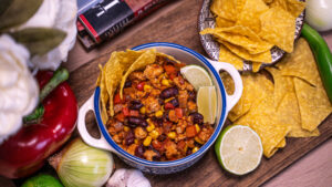 Chilli cu carne de curcan servit într-un bol decorativ, alături de tortilla chips și lime proaspăt.